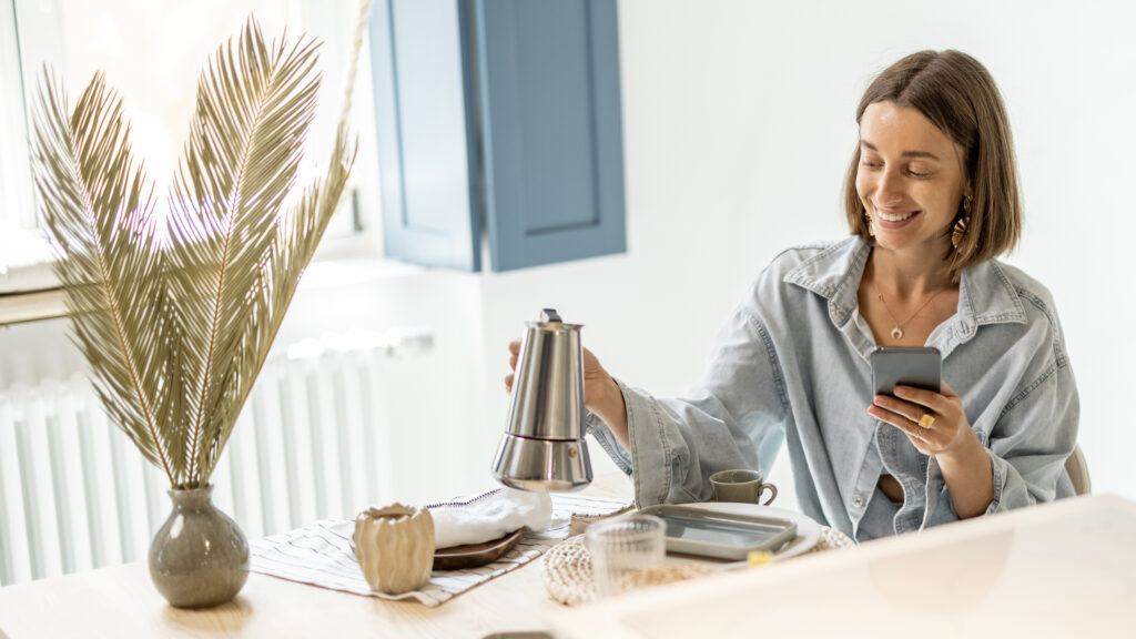 woman on phone pouring coffee at home