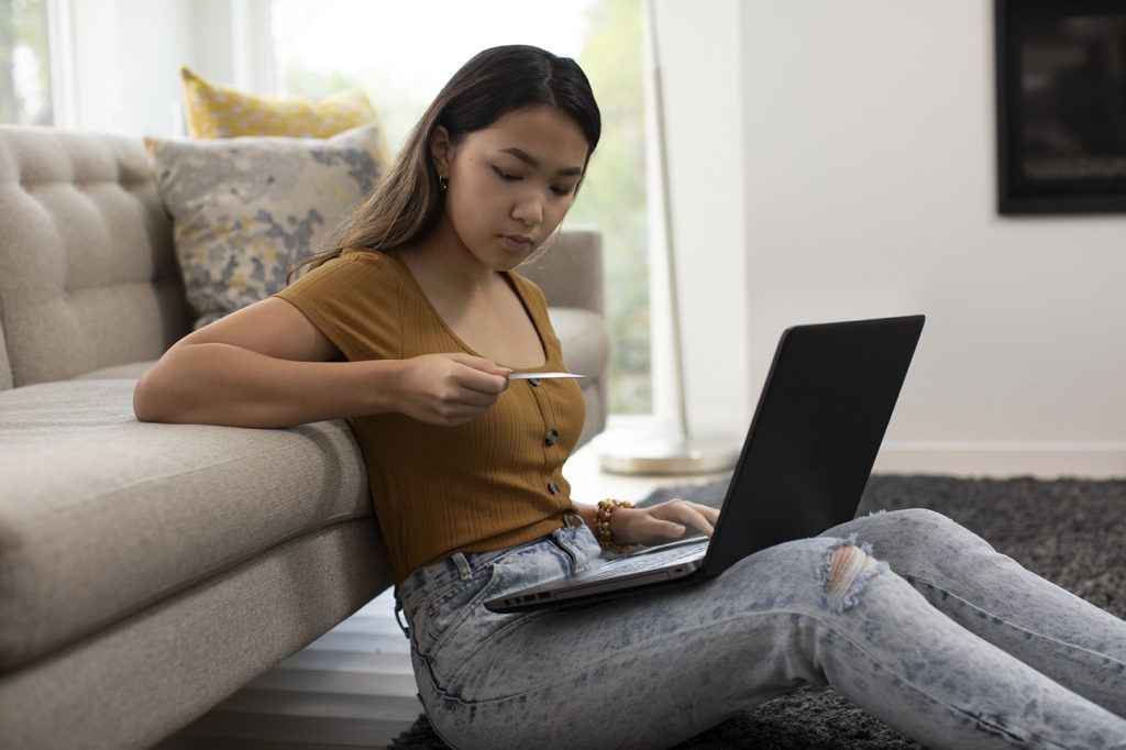 Woman sitting on floor in living room using her laptop to pay a bill while holding her credit card