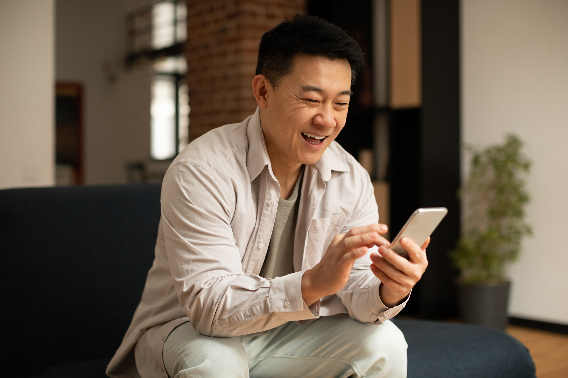 Asian middle aged man chatting on smartphone or surfing internet while resting on sofa in living