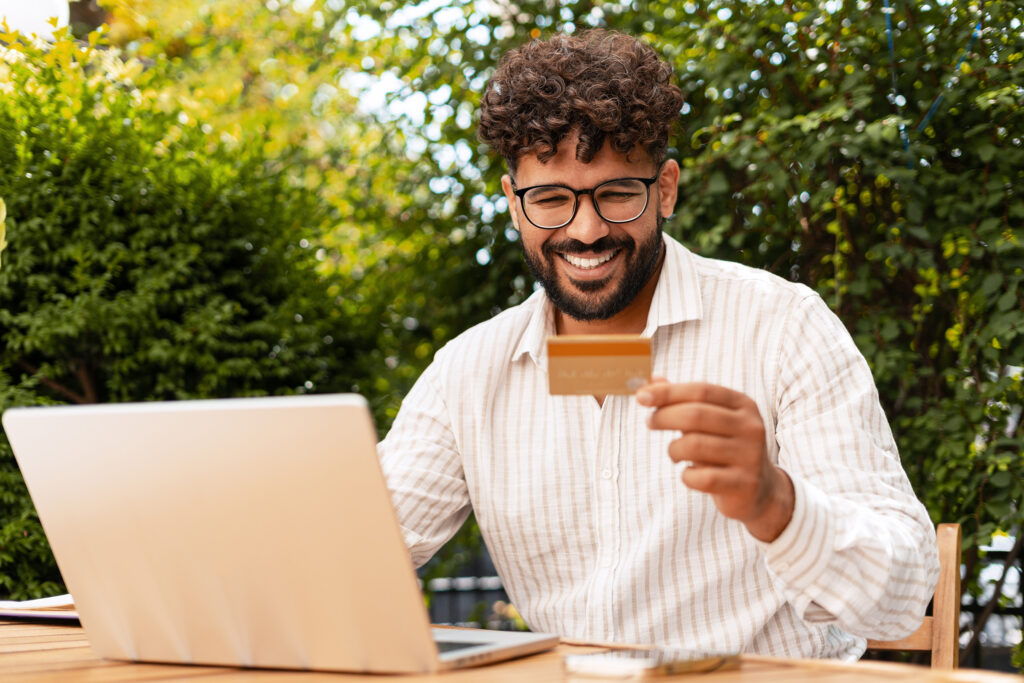 Freelancer smiling and buying online with credit card and laptop in the garden