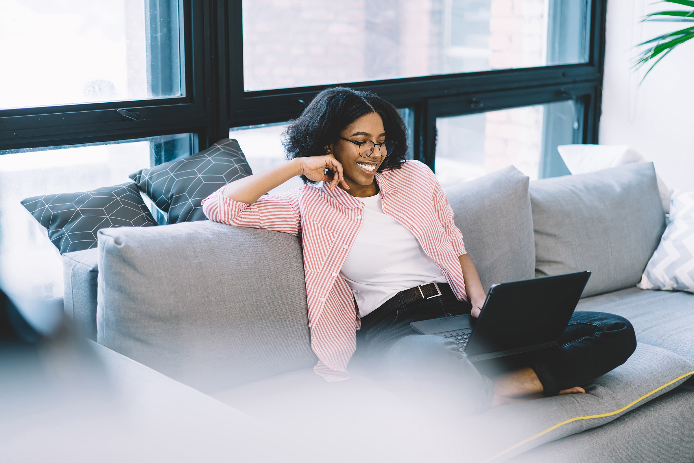 happy dark skinned woman watching funny movie on laptop while resting at comfortable sofa