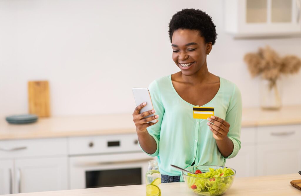 Woman in kitchen shopping with phone and credit card