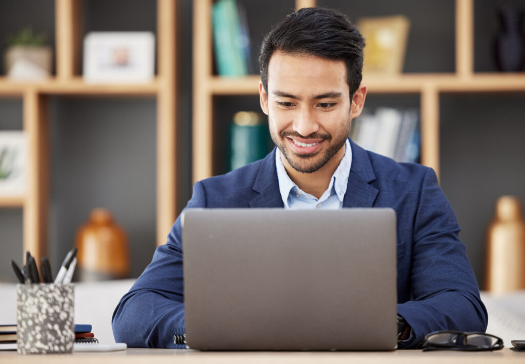 man in office with laptop smiling and typing email