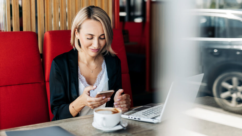 Woman in cafe using phone and laptop