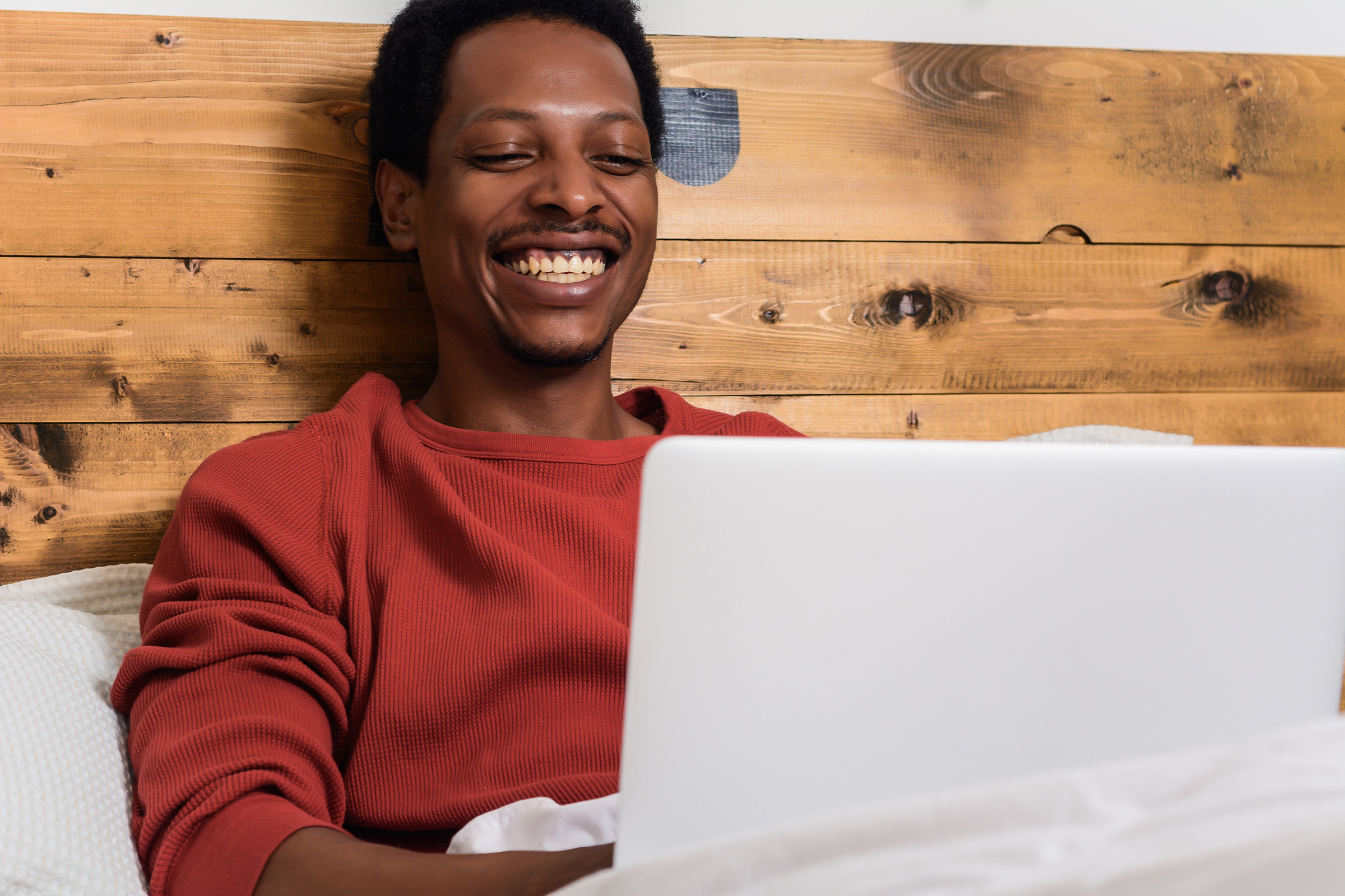 Young Afro American Man Using His Laptop In Bed.