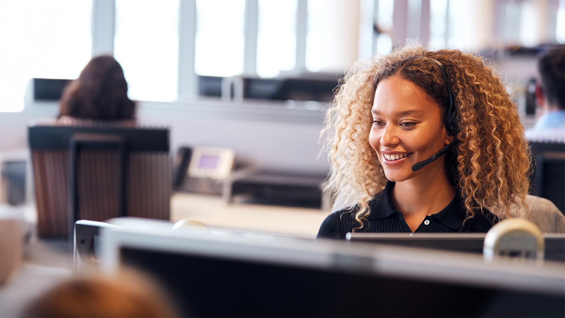 Young Businesswoman Wearing Telephone Headset Talking To Caller In Customer Services Department